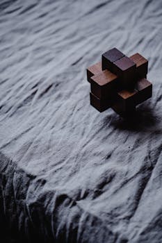 Close-up of a wooden puzzle resting on a textured cloth background, evoking a sense of mystery and focus.