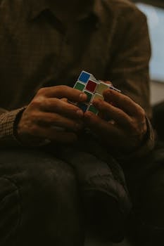 Close-up of hands focusing on solving a Rubik's Cube indoors, showcasing concentration and skill.