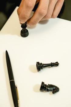 Hand holding chess piece on white surface, depicting strategic planning.