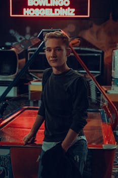 Portrait of a young man posing in a neon-lit arcade with retro vibes.